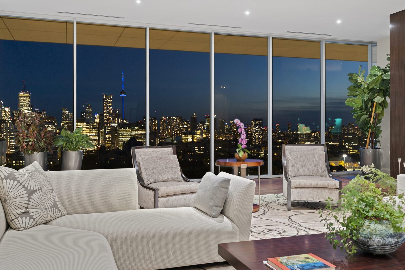 Penthouse interior at dusk with the Toronto skyline glowing through glass walls